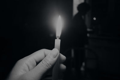 Cropped hand holding illuminated candle