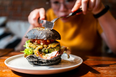 Hands cuts broccoli quinoa charcoal burger topped with guacamole, mango salsa and fresh salad.