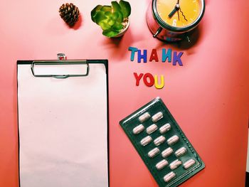 Directly above shot of clipboard with thank you message by clock on table