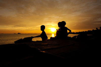 Silhouette boys on beach against sky during sunset