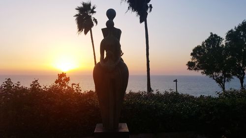 Silhouette woman standing by sea against sky during sunset