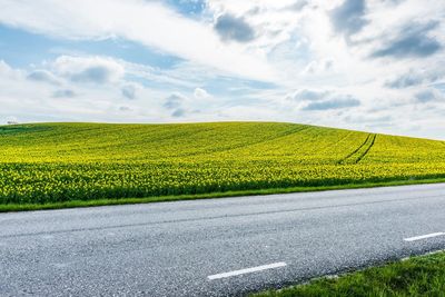 Road passing through field against cloudy sky