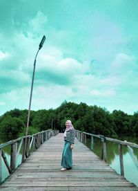 Rear view of woman standing on bridge against sky