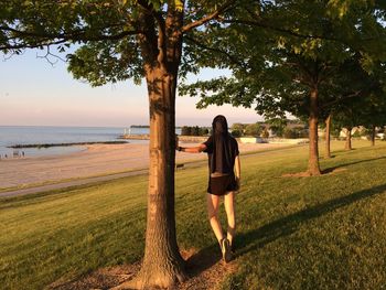 Full length rear view of man on tree trunk against sky