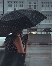 Rear view of man holding umbrella on street in rainy season