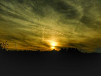Silhouette trees on field against dramatic sky