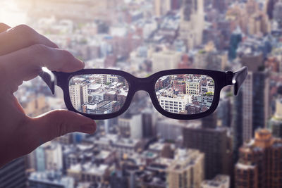 Close-up of hand holding eyeglasses against cityscape