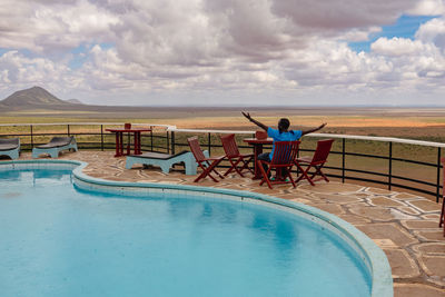 A man sitting next to a swimming pool against a scenic lookout at tsavo east national park in kenya