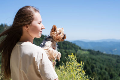 Young woman holding small dog puppy yorkshire terrier hiking at the mountains
