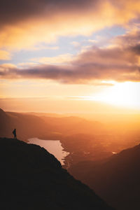 Silhouette person standing on mountain against sky during sunset