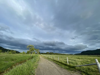 Empty road amidst field against sky