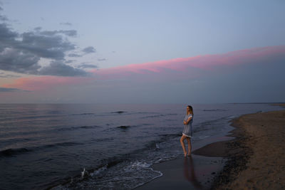 Woman standing on beach against sky during sunset