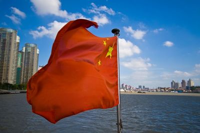Chinese flag by sea in city against sky