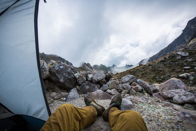 Low section of man relaxing on mountain against sky