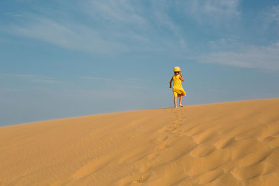 Rear view of woman walking on sand at desert against sky