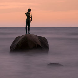 Full length of man standing on rock at beach during sunset