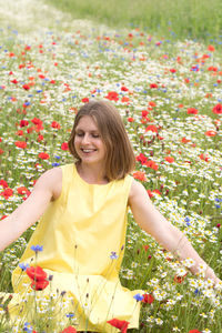 A beautiful young blonde woman in a yellow dress stands among a flowering field