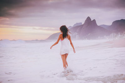 Rear view of woman walking on shore during sunset