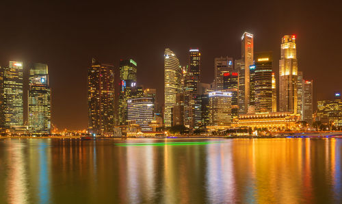 Illuminated buildings by river against sky at night