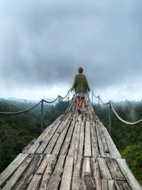 Rear view of woman standing on footbridge against sky