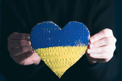 Cropped hand holding heart shape against black background