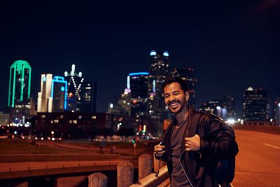 Portrait of smiling young man standing in city at night