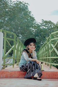 Woman looking away while sitting on railing against plants