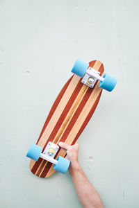 Crop unrecognizable male skater demonstrating handmade penny board with blue wheels against light wall in daytime