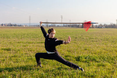 Caucasian young woman practicing wushu martial art on a green meadow with a long spear