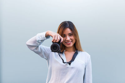 Young woman holding camera against wall