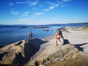 Woman looking at people in sea against blue sky