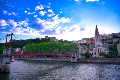 Bridge over river amidst buildings in city against sky