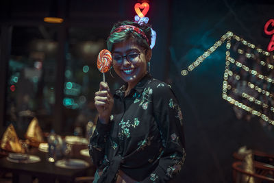 Full length of a smiling young woman holding illuminated lights at night