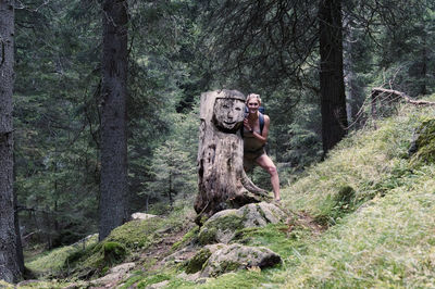 Portrait of woman standing by tree trunk in forest