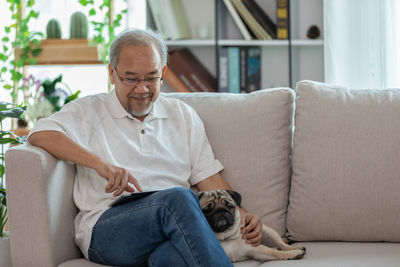 Cheerful man using digital tablet while sitting with dog on sofa