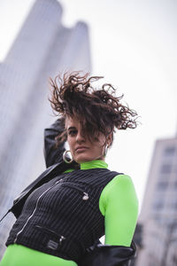 Portrait of woman with tousled hair standing against buildings in city