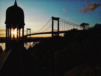Silhouette of bridge over river against cloudy sky