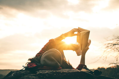 Woman reading book while lying on lakeshore during sunset