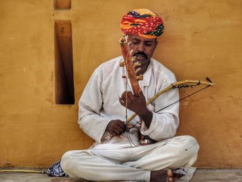 Man playing with violin while sitting against wall