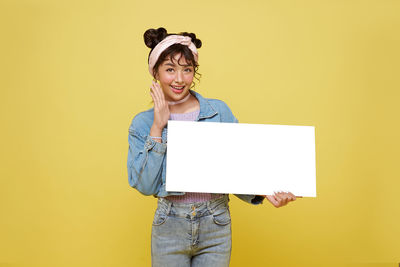 Portrait of smiling young woman standing against yellow background