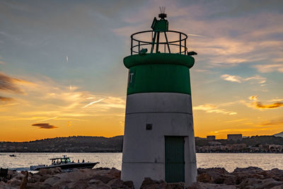 Lighthouse by sea against sky during sunset