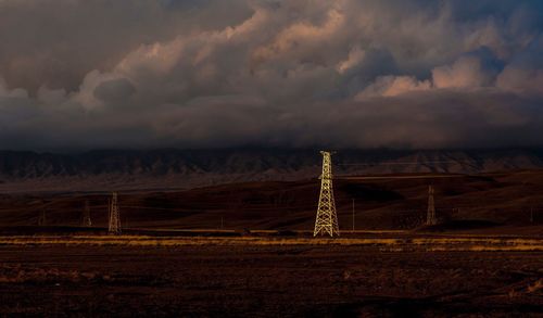 Electricity pylons on landscape against cloudy sky