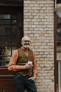 Portrait of happy male owner with coffee cup standing outside store