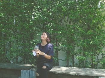 Young woman relaxing with drink on bench against trees