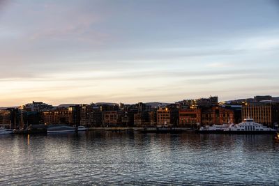 River by buildings against sky during sunset in city