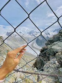 Cropped image of person hand holding fence against sky