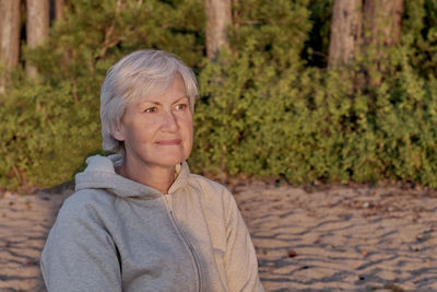 Portrait of thoughtful senior woman with short gray hair  against backdrop of nature in sunset light