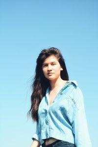 Portrait of young woman standing against clear blue sky