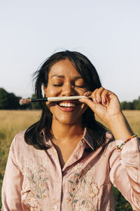 Smiling woman with eyes closed holding paintbrush during sunny day