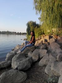 Woman sitting on rock against sky